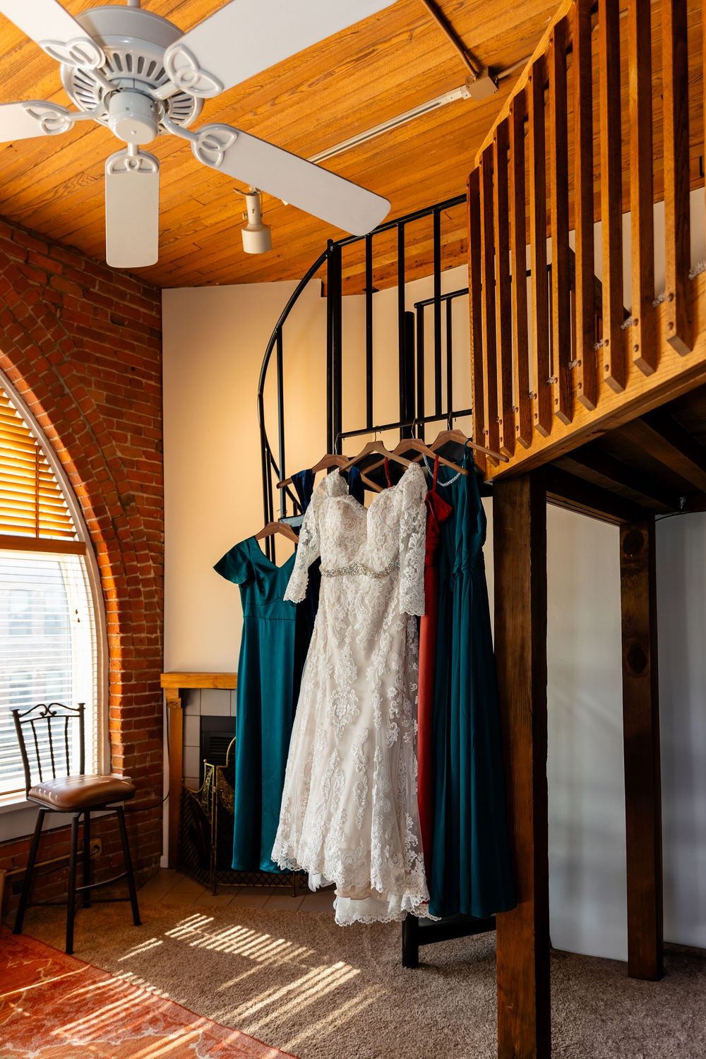 Wedding dresses and teal bridesmaid gowns hanging on a railing in a rustic brick Air BNB with wood ceiling in Omaha, NE