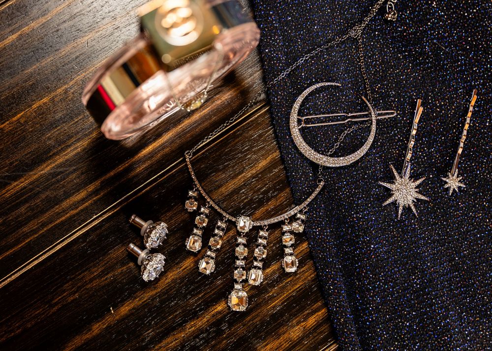 Sparkling crystal jewelry and accessories arranged on a dark wooden surface with perfume bottle.