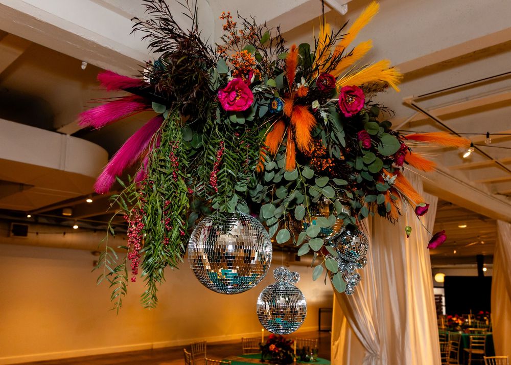 Colorful floral arrangement with feathers and disco balls hanging from ceiling at wedding reception.