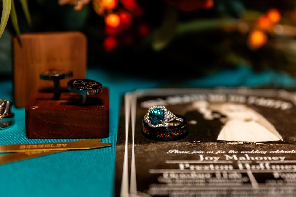Elegant wedding details with teal gemstone ring, cufflinks on wood box, and wedding invitation on teal fabric.