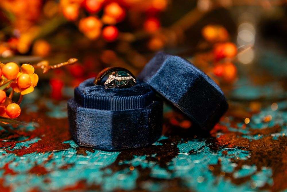 Gold diamond engagement ring displayed in a navy blue velvet ring box with autumn berries in background.