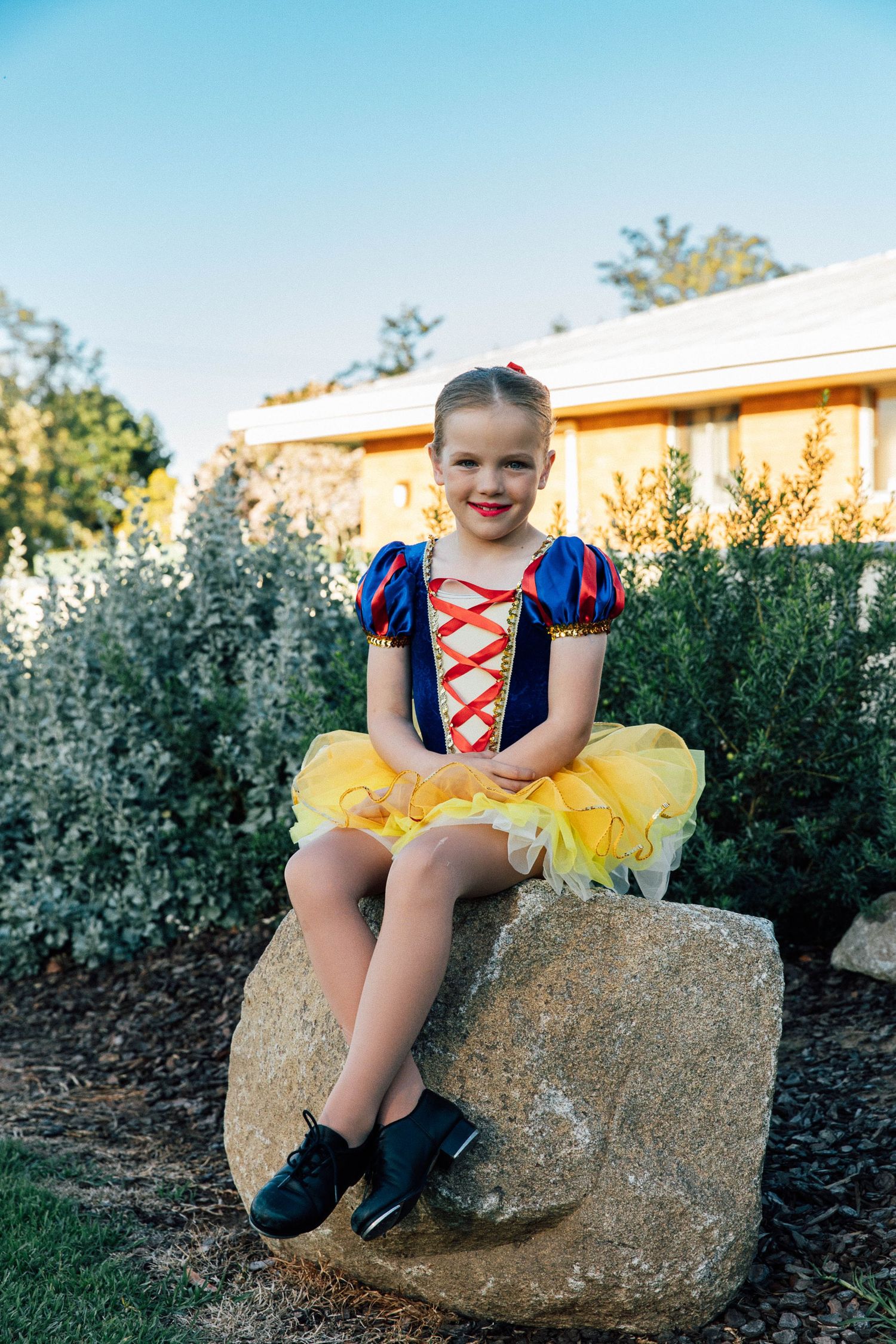 Little girl sitting on a rock in a garden in a playground during a dance costume photo shoot.