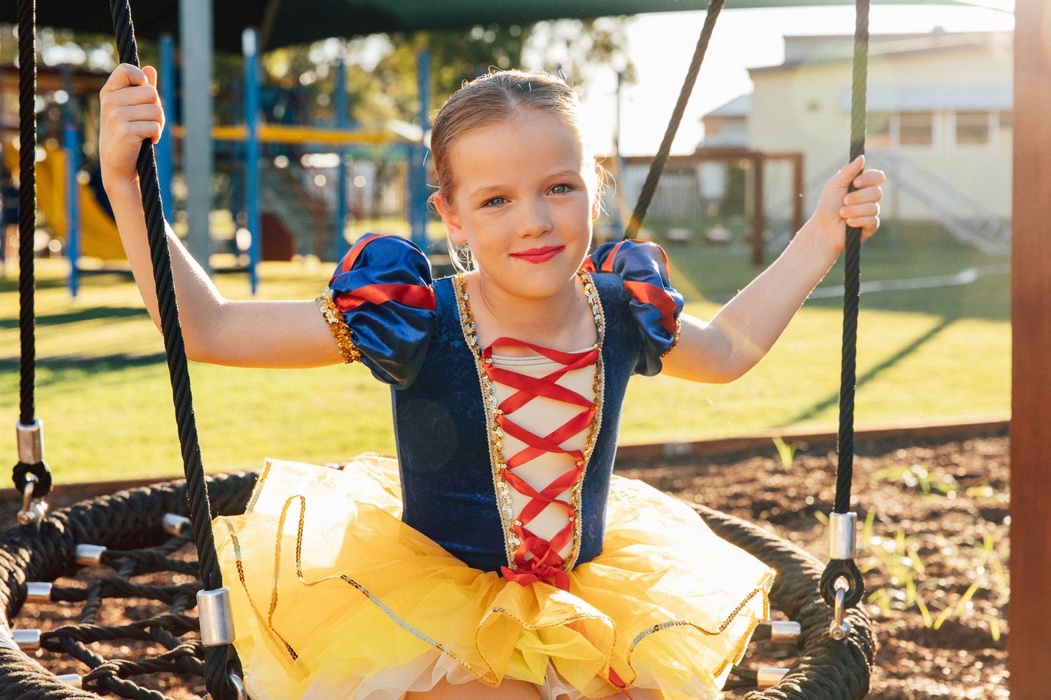 Little girl sitting on a swing in a playground during a dance costume photo shoot.