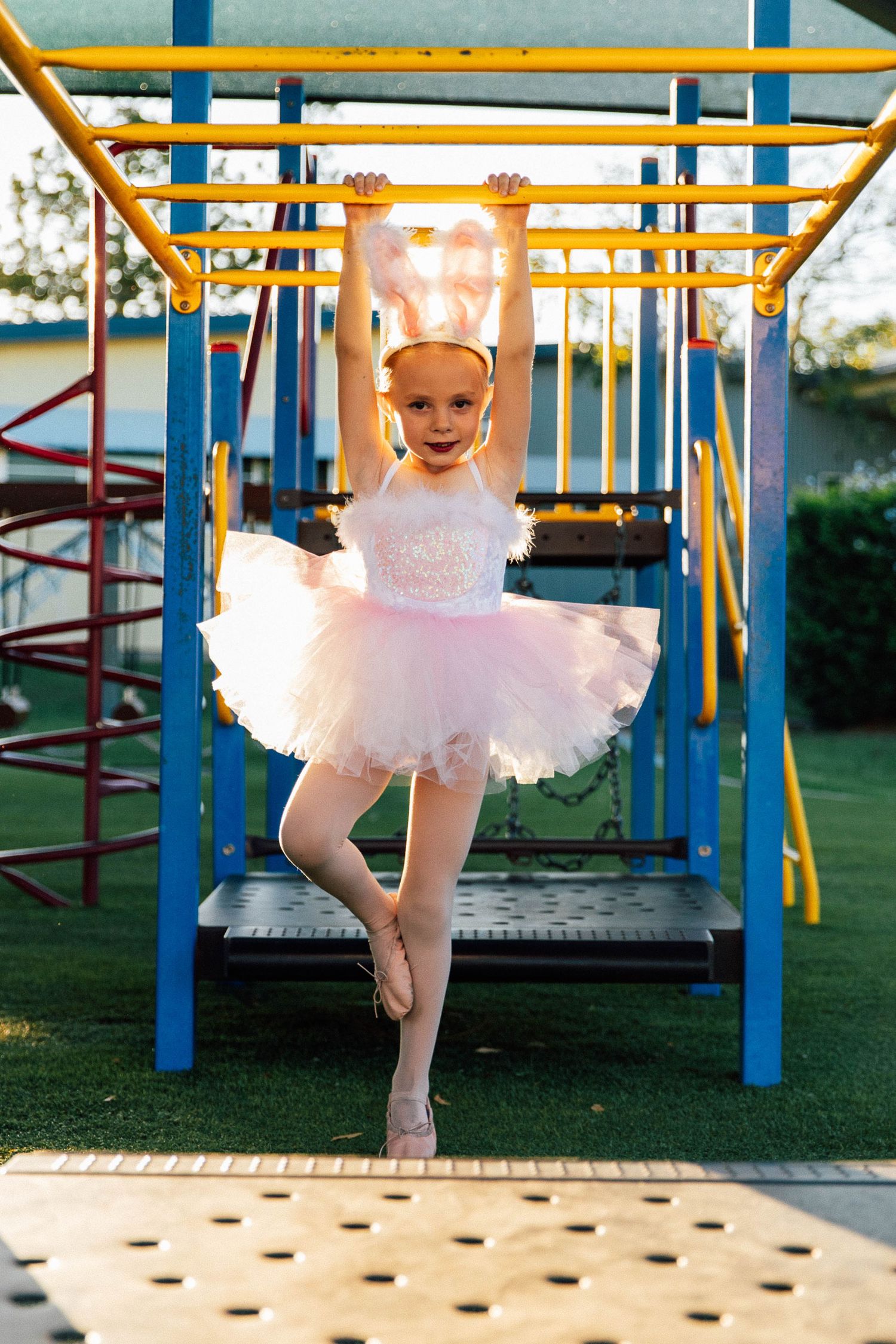 Little girl hanging from monkey bars on a playground during a dance costume photo shoot.