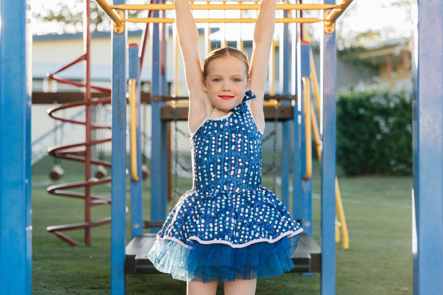 Little girl swinging on the monkey bars in a playground during a dance costume photo shoot.