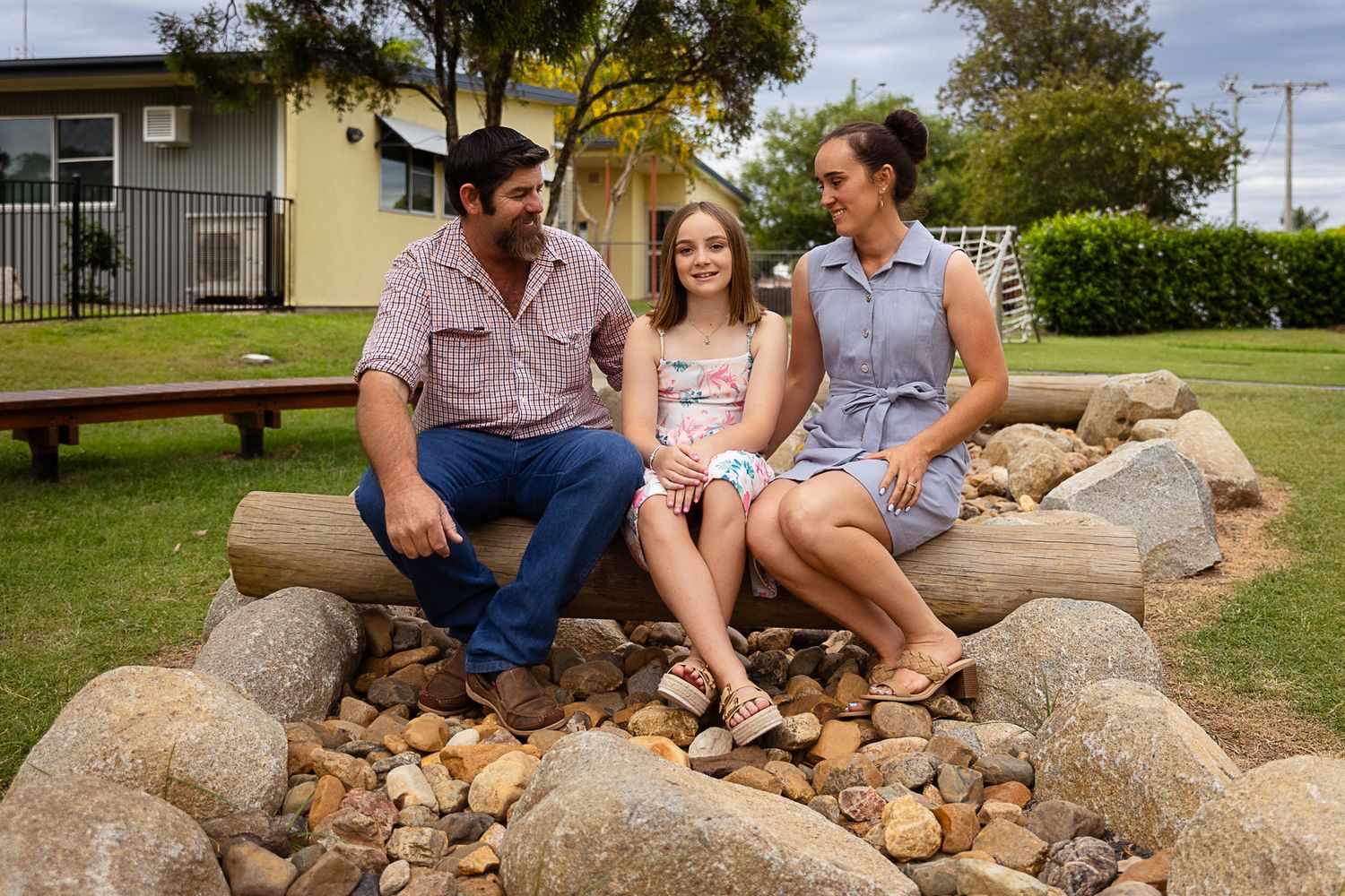 Little girl and parents sitting on a log in a creek in a playground during a dance costume photo shoot.