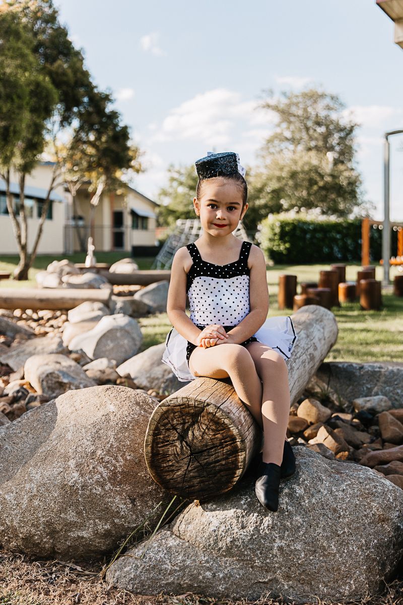 Little girl sitting on a log in a creek in a playground during a dance costume photo shoot.