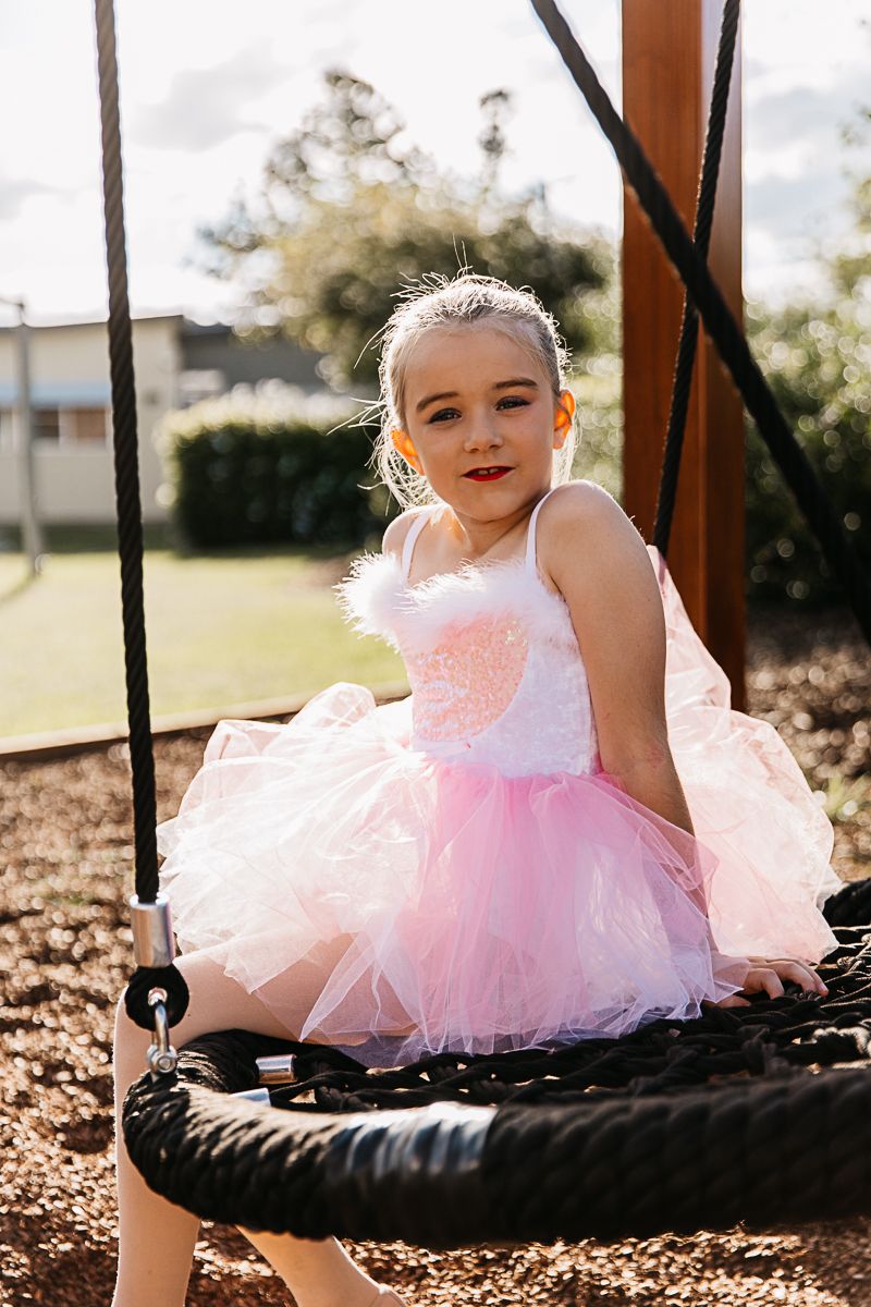 Little girl sitting on a swing in the playground during a dance costume photo shoot.