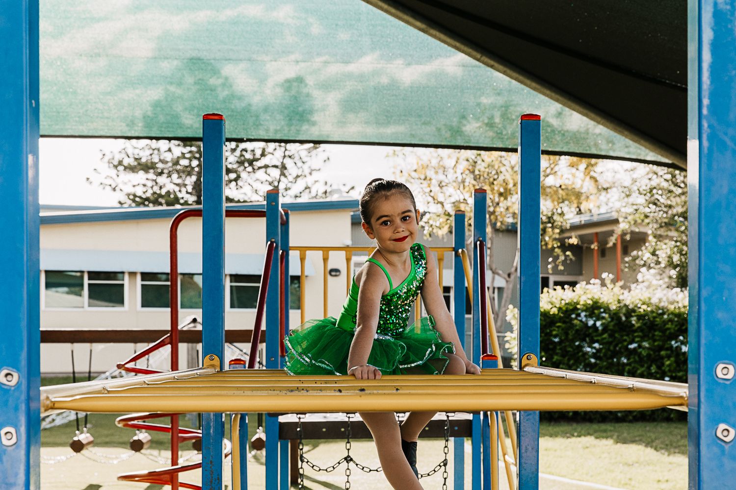 Little girl sitting on the monkey bars on a playground during a dance costume photo shoot.