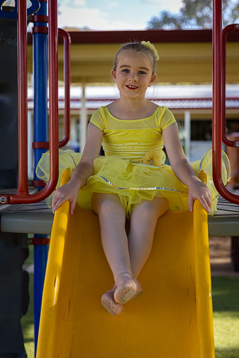 Little girl sitting on a slide in a playground during a dance costume photo shoot.