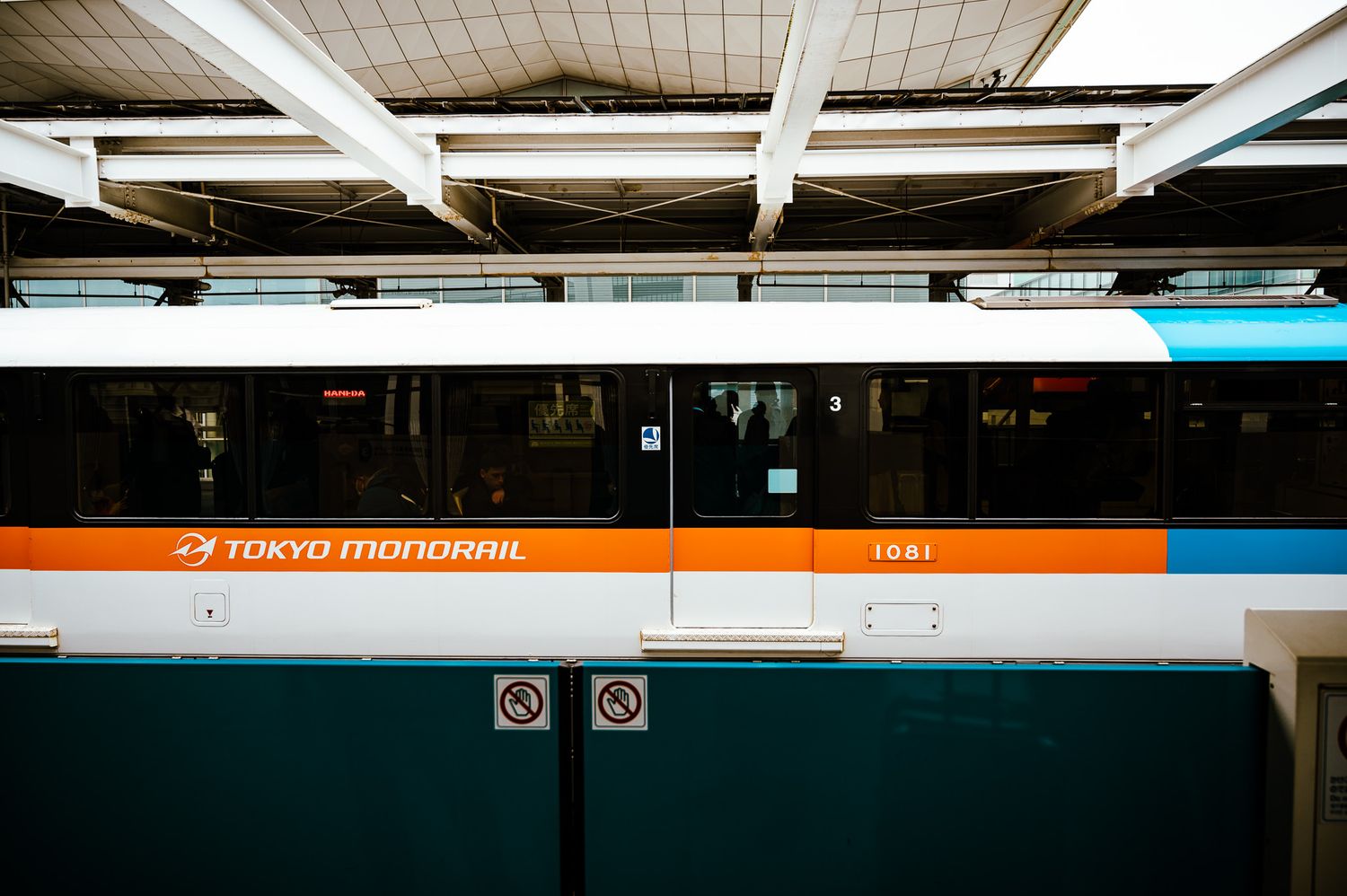 Tokyo Monorail train in teal, orange, and white colors stopped at a station platform in Japan.