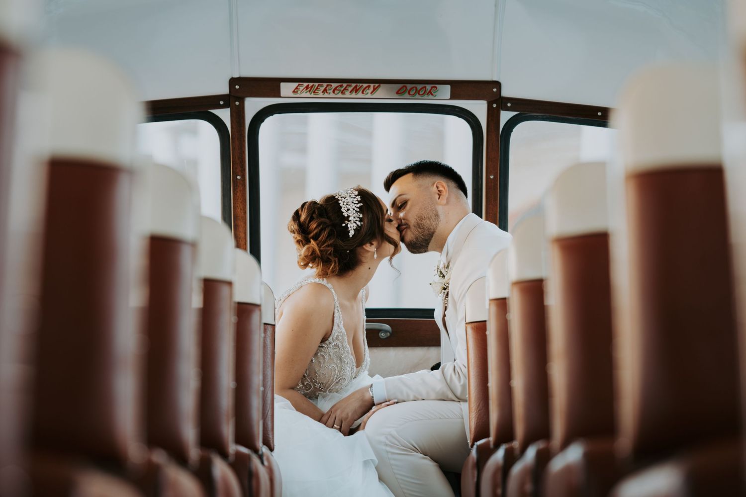A couple in wedding attire embraces in front of a row of wooden columns at an elegant venue.