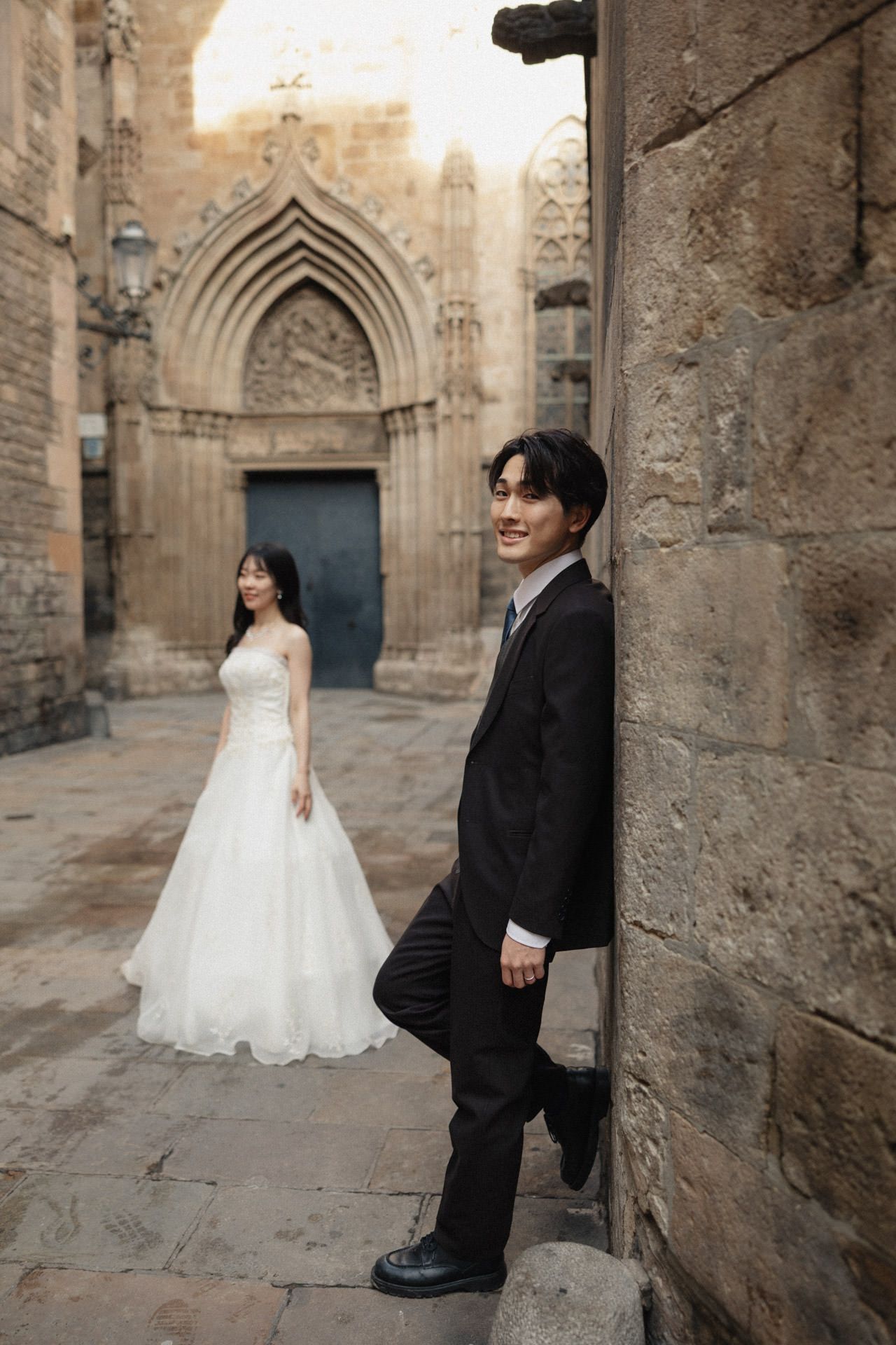 A bride and groom pose for romantic wedding photos against the stone walls and Gothic architecture of an ancient church.