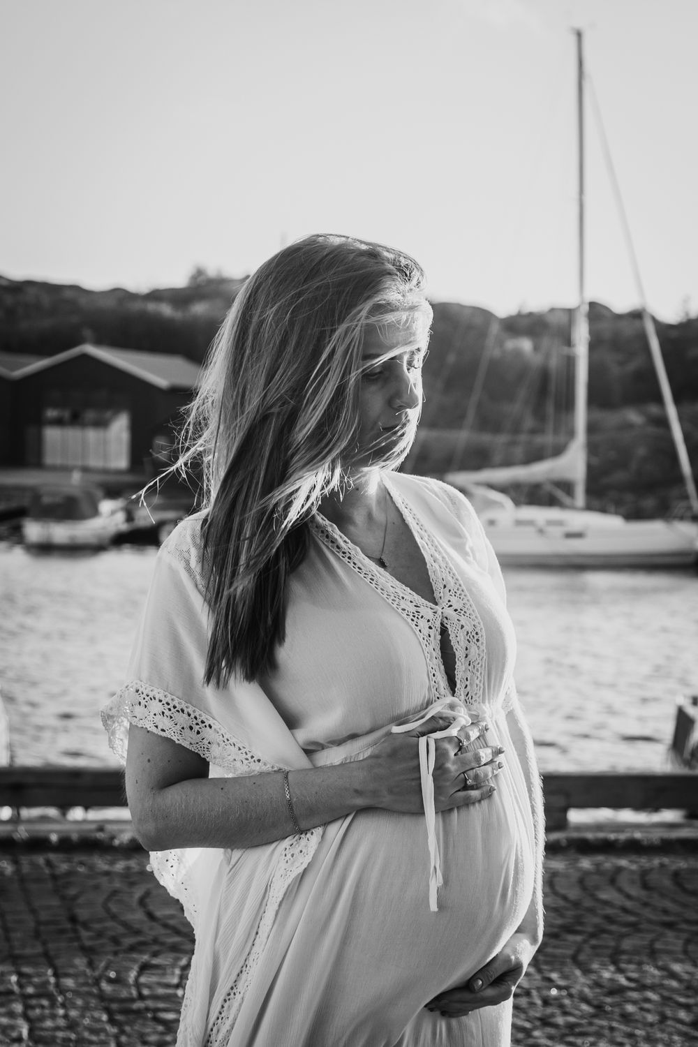 Black and white triptych of a person in a white dress standing near a harbor with boats in the background.