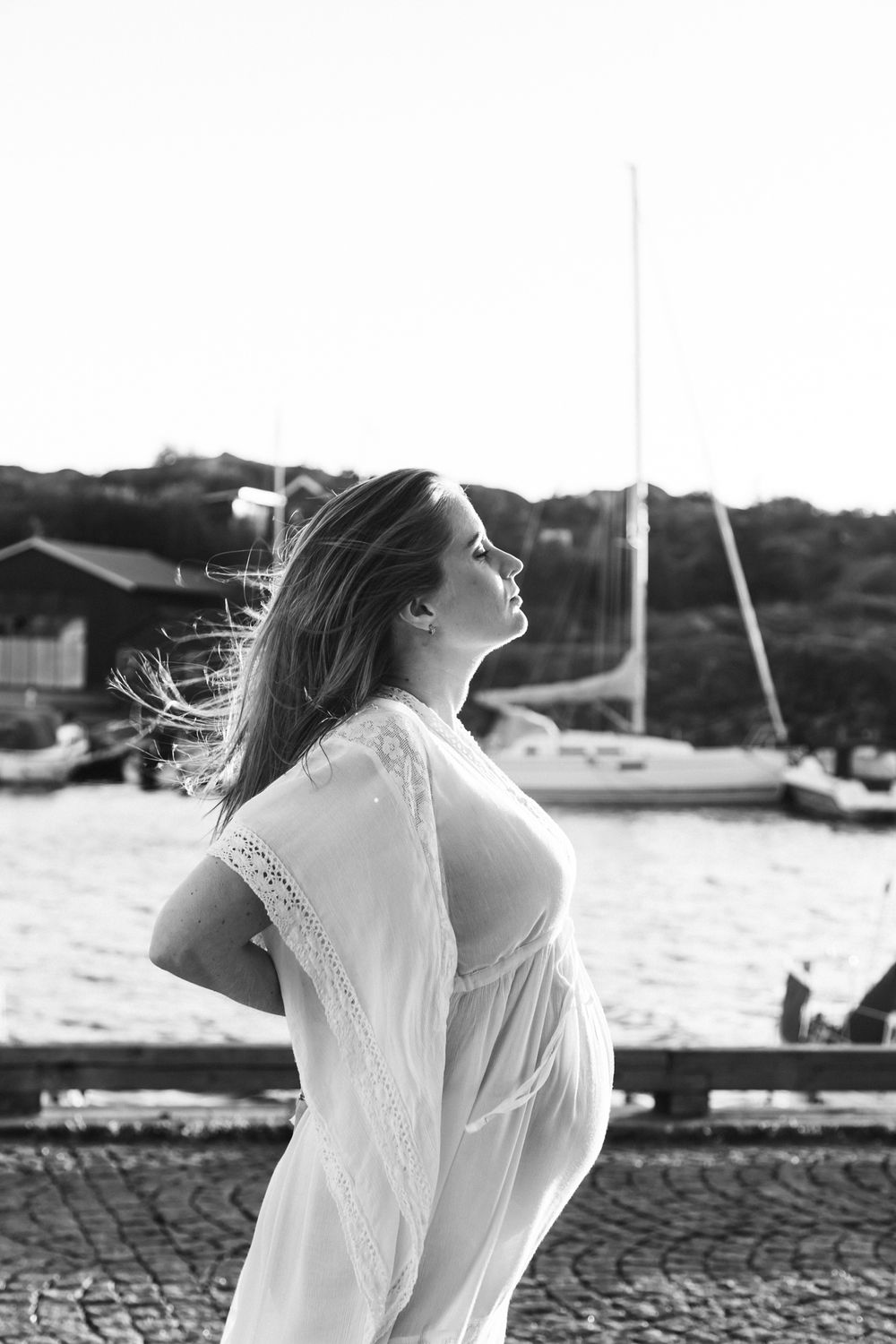 A person in a white dress stands by the water, with their hair flowing in the wind in three similar black and white photos.