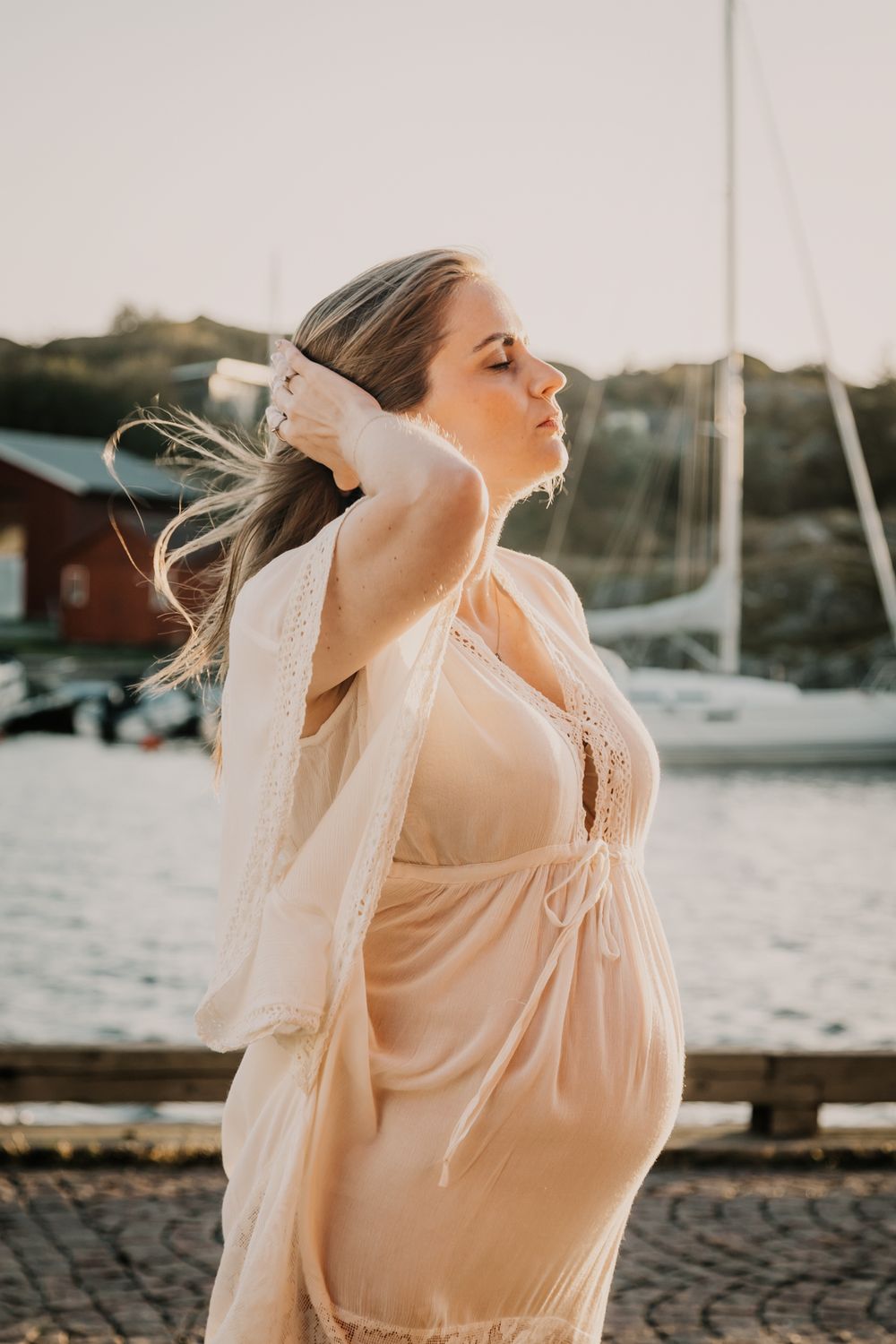 A bride in a flowing white dress and veil dances joyfully by the waterfront at sunset.