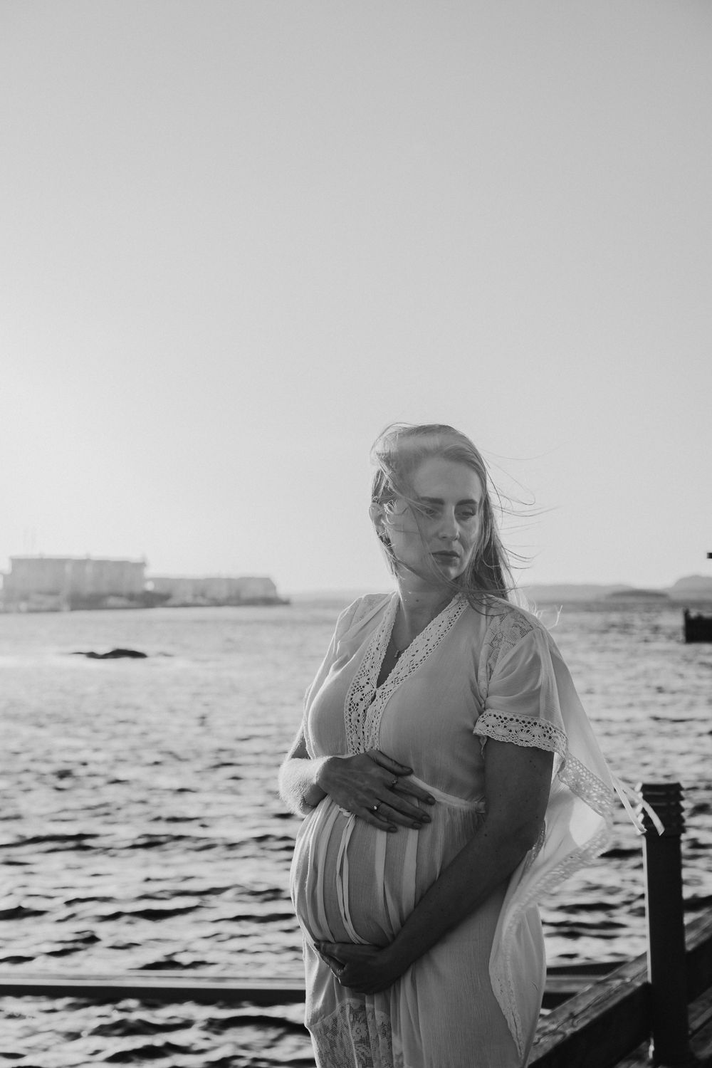 A black and white photo series shows a couple embracing by the water at sunset in romantic seaside moments.