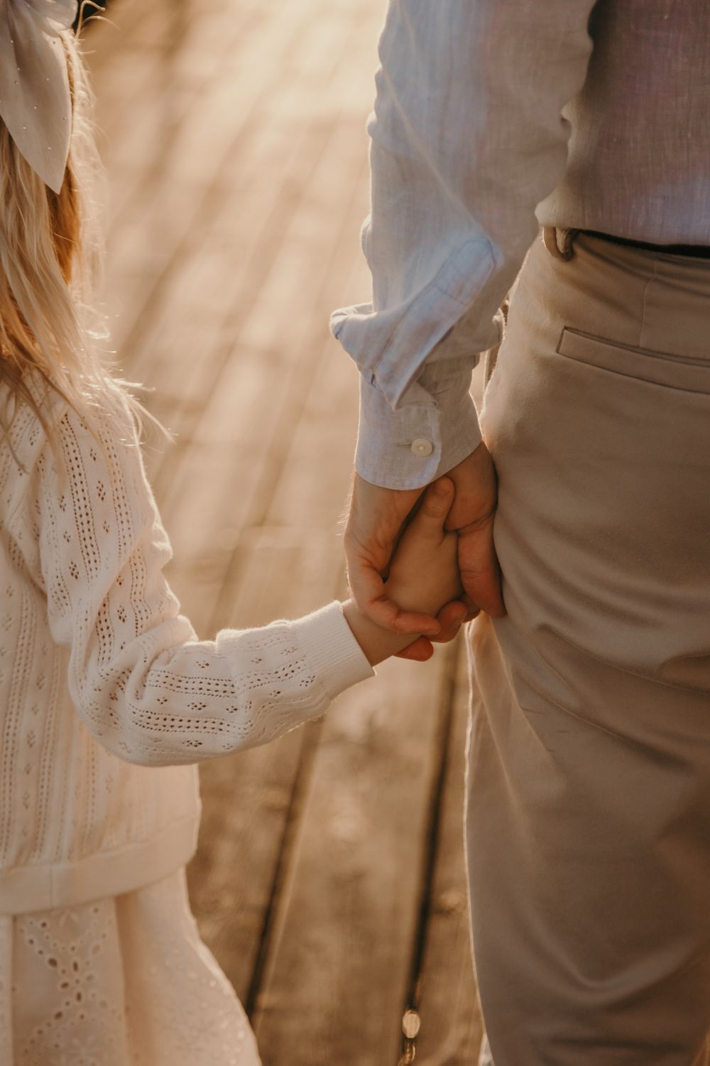 Couple holding hands wearing white and beige outfits in romantic sunset lighting.