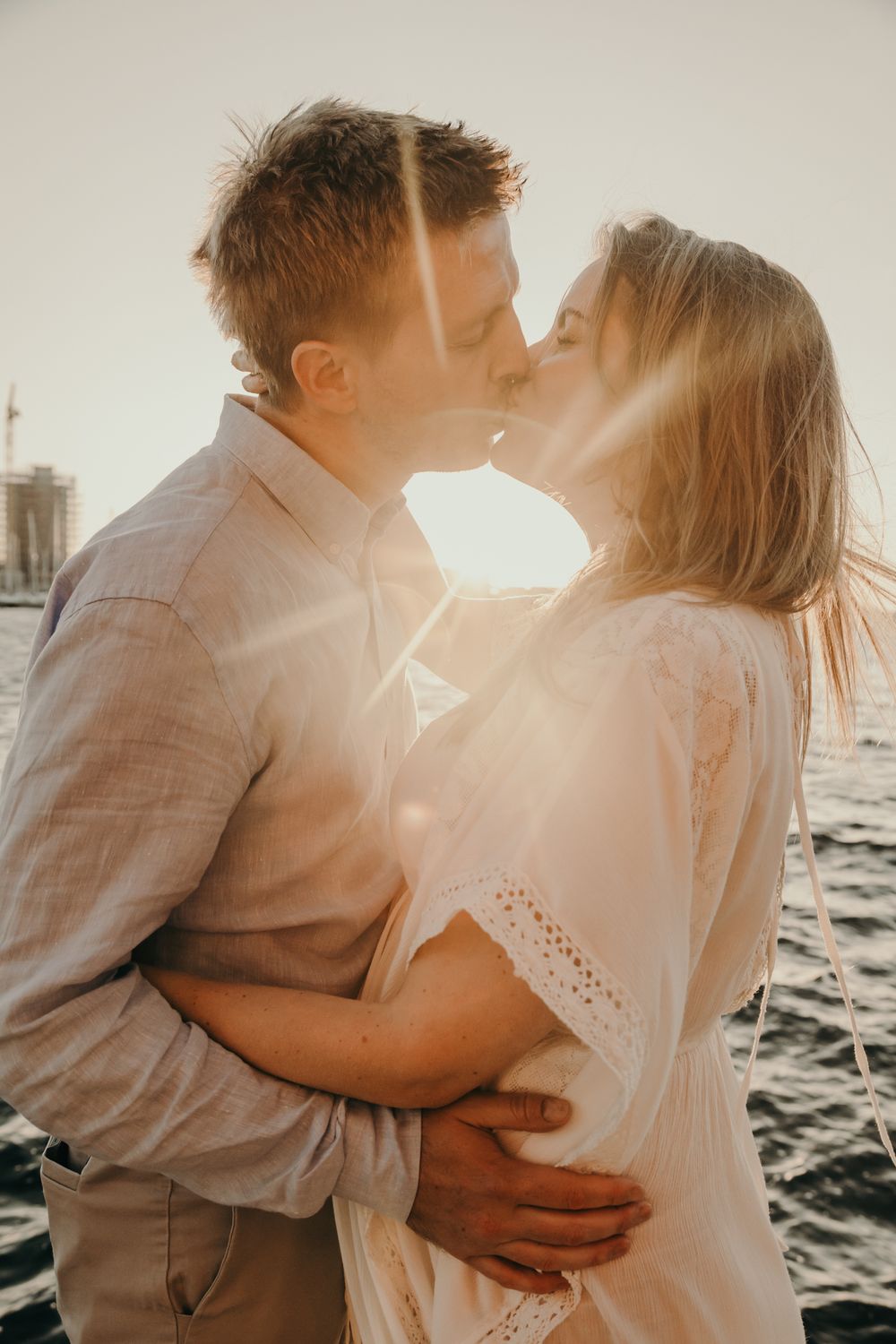 Romantic couple in white embracing by the water during sunset.