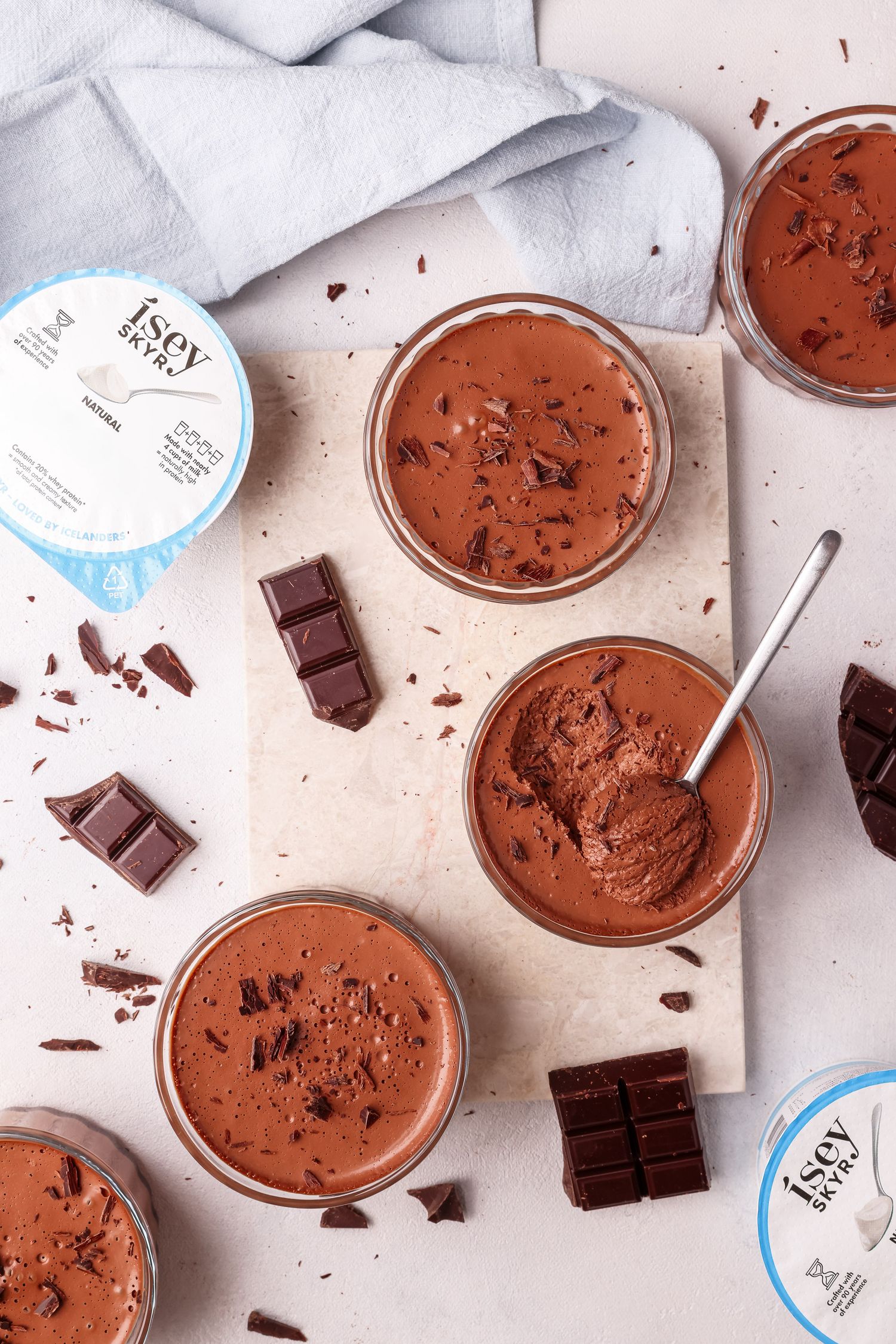 Chocolate mousse desserts in glass jars with dark chocolate chunks scattered on a light surface.
