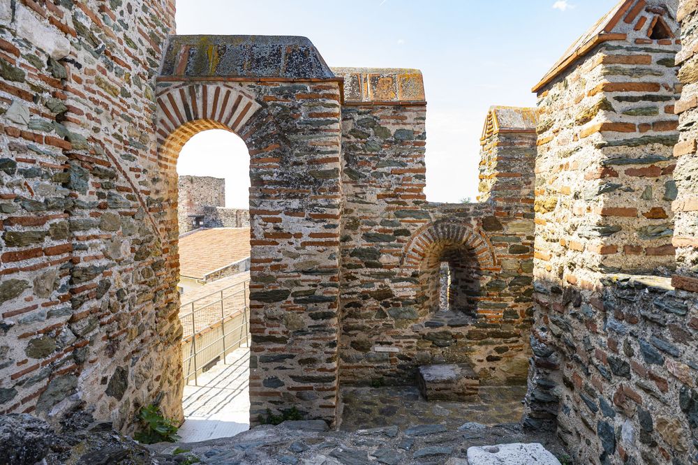 Ancient stone archway and walls of a historic fortress with sunlight streaming through the opening.