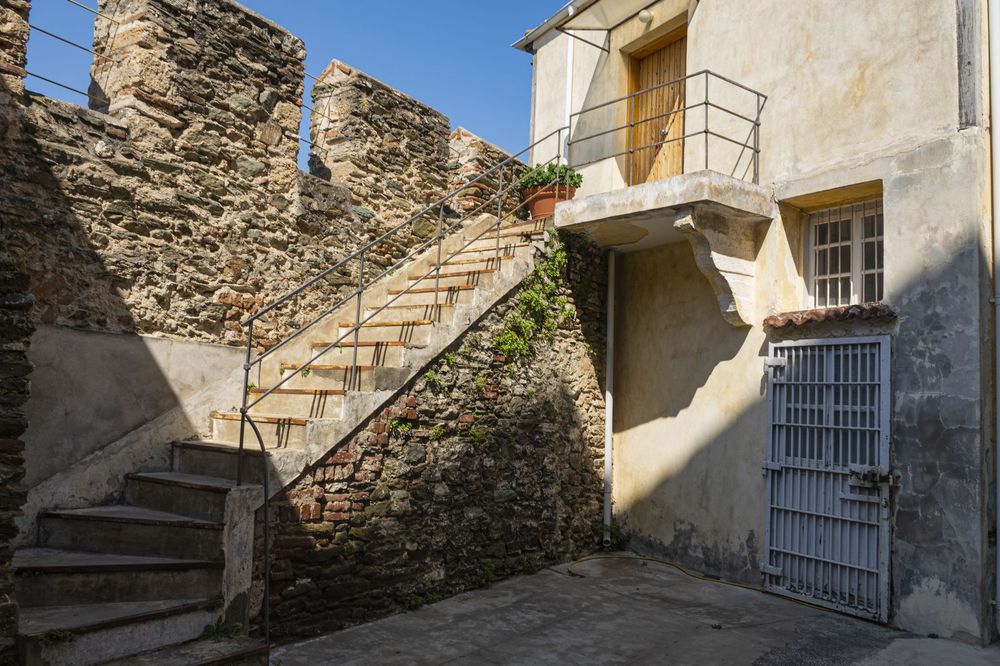 Stone walls and steps lead up a narrow alley between historic buildings in a Mediterranean village.