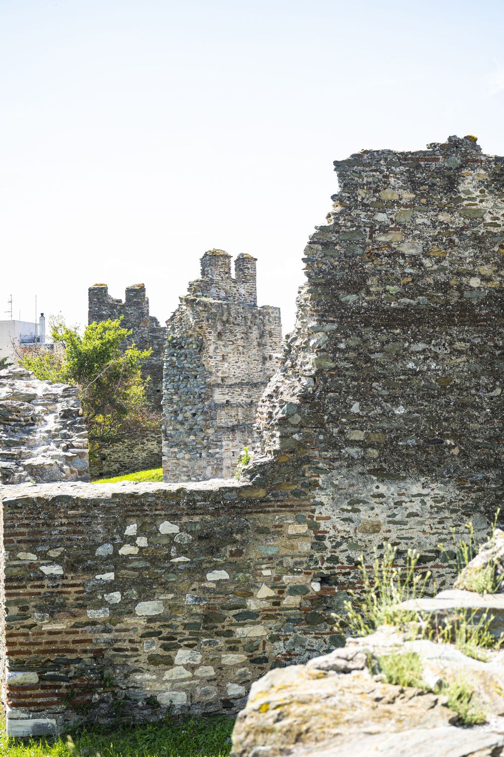 Ancient stone wall ruins with crumbling masonry and vegetation growing among the weathered stones in bright sunlight.