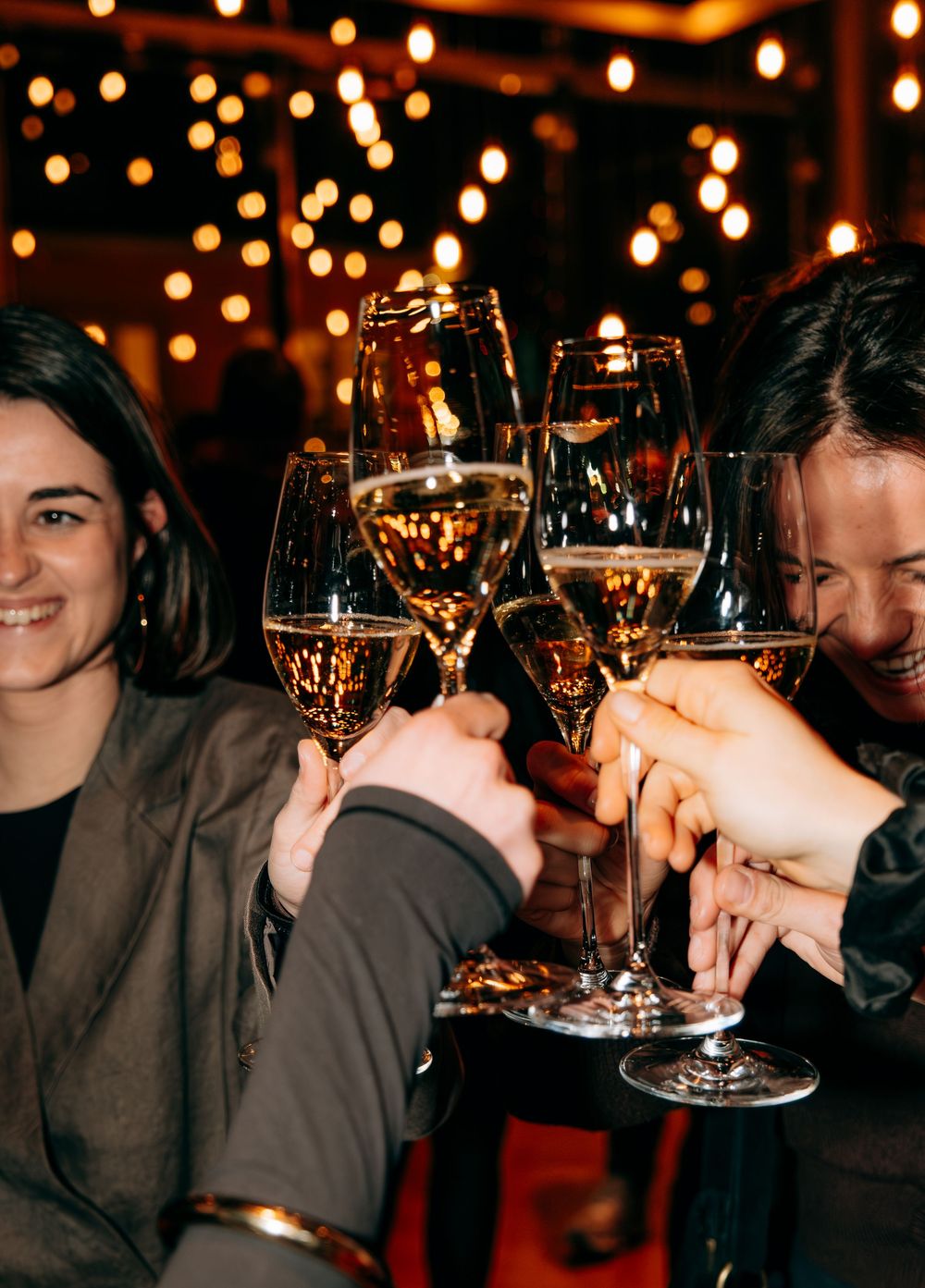 Group of people toasting with champagne glasses at a warmly lit celebration dinner.