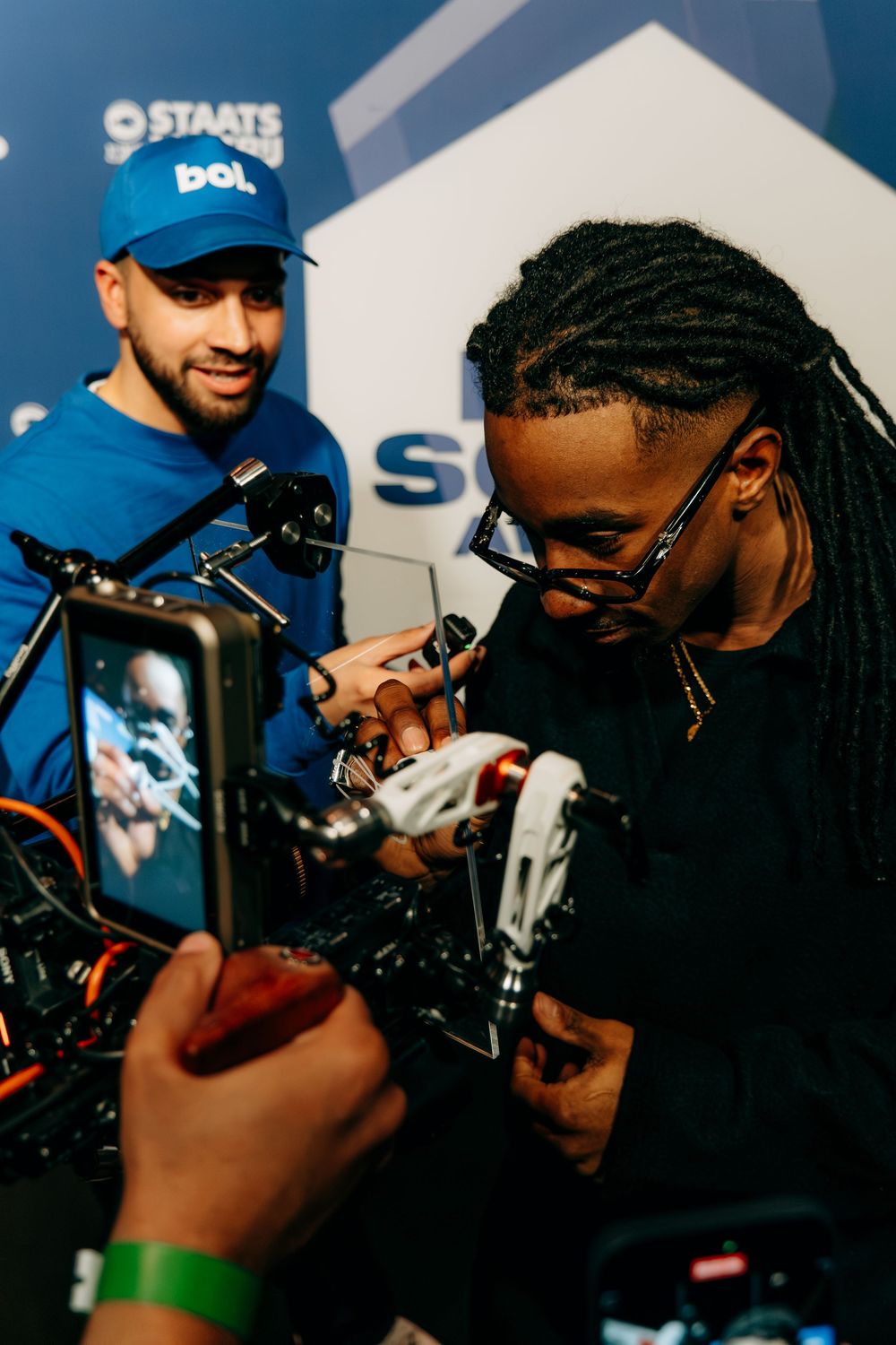 Two men examining camera equipment at bol.com branded event, one wearing blue bol.com cap.