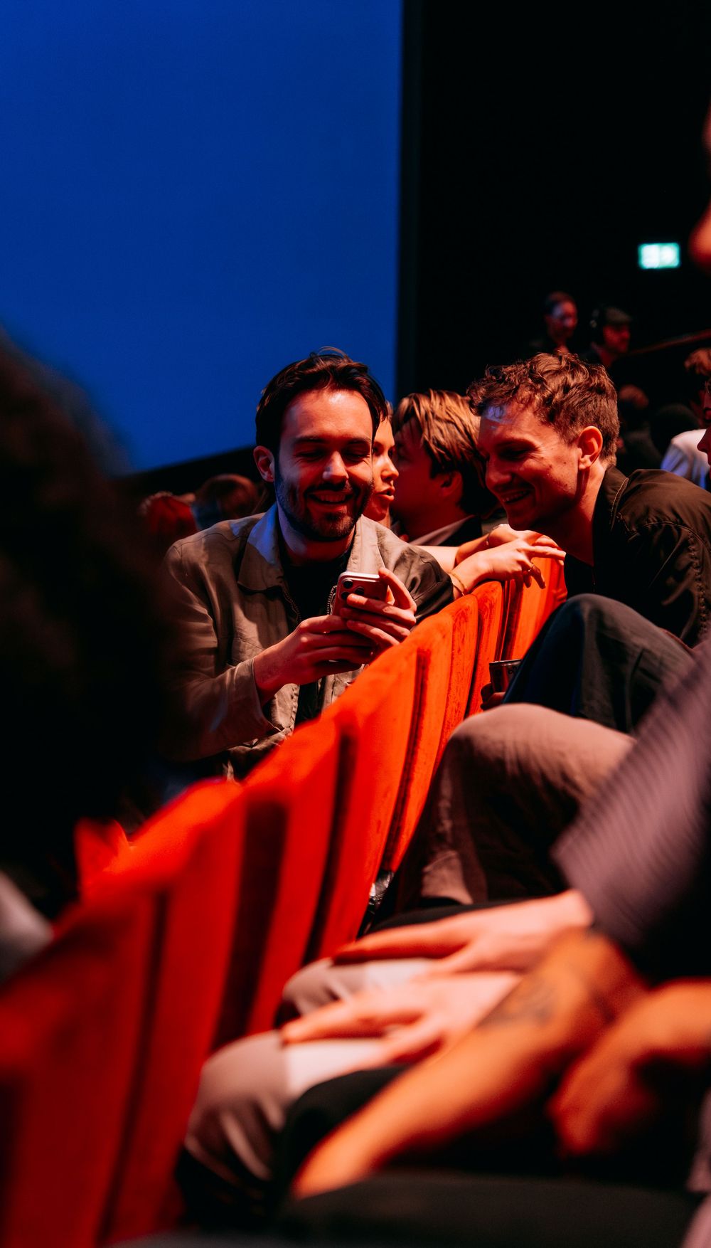 Two men chatting and smiling in theater seats at an awards event.
