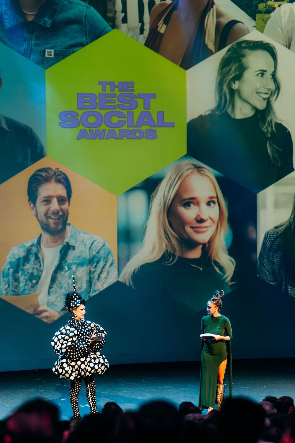 Two hosts on stage at The Best Social Awards with nominee photos displayed on screen.