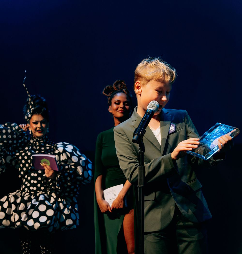 Young blonde winner accepting award on stage at The Best Social Awards ceremony.