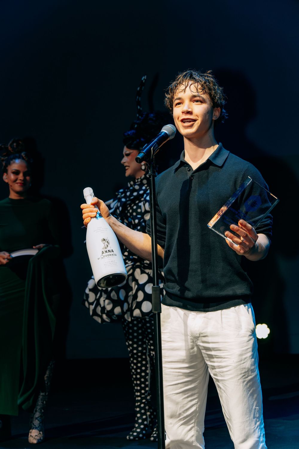 Young man holding a bottle of wine and a glass award trophy on stage.