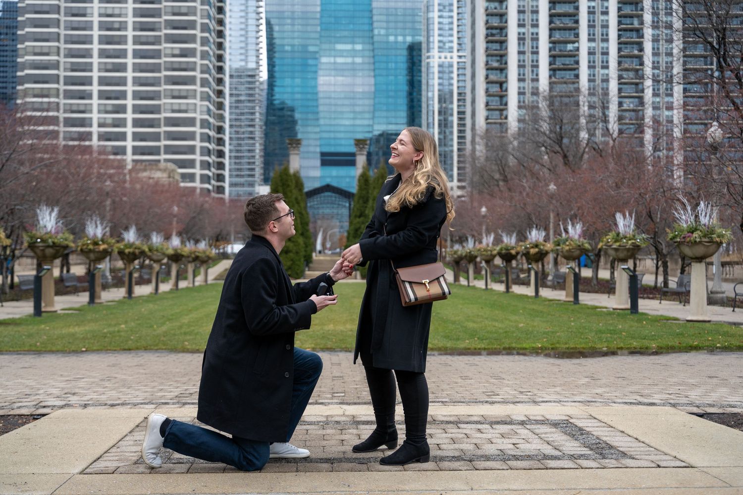 A series of photos showing a proposal moment along a city waterfront park with skyscrapers in the background.