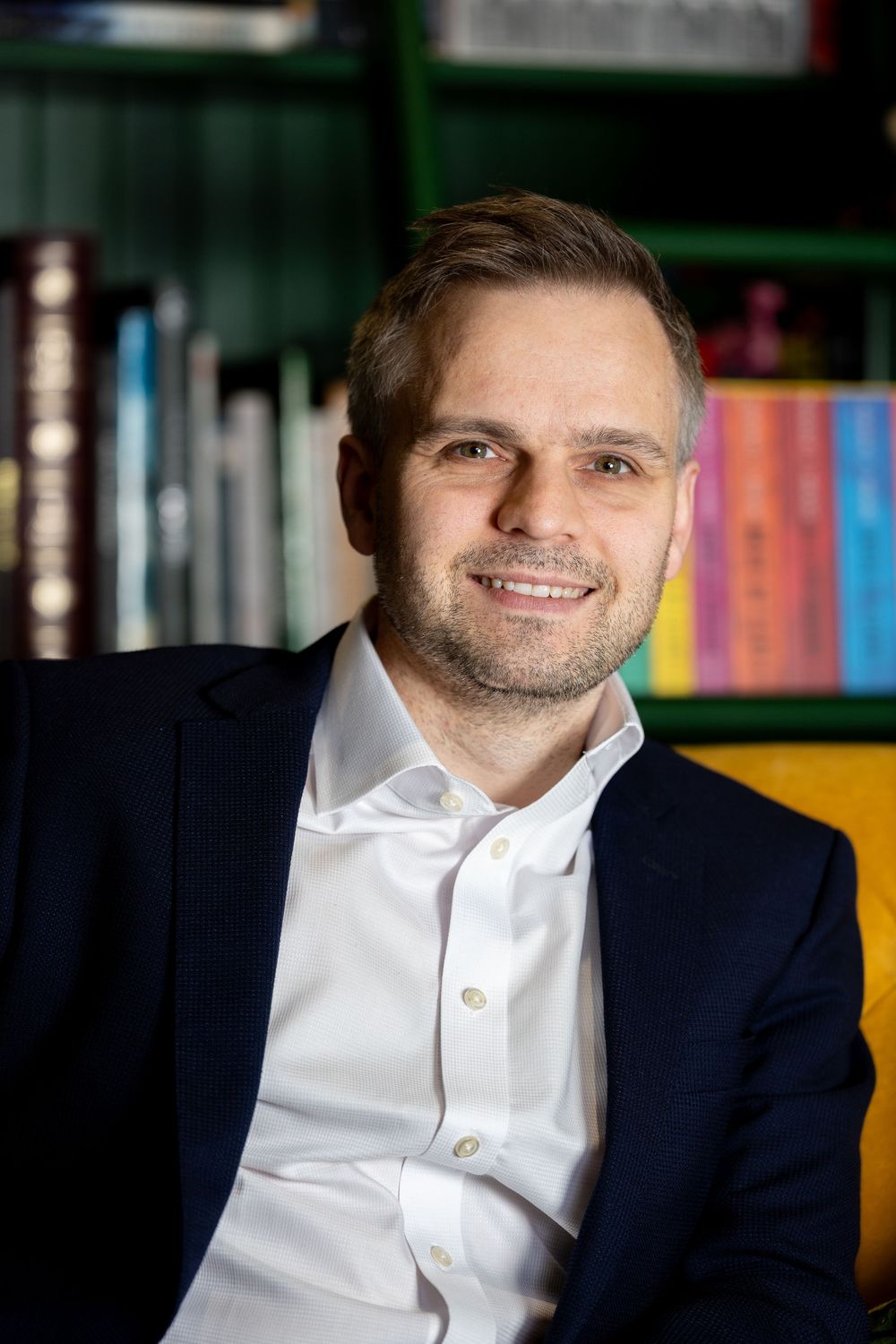 Professional portrait series of a person in a navy blazer and white shirt against a blurred bookshelf background.