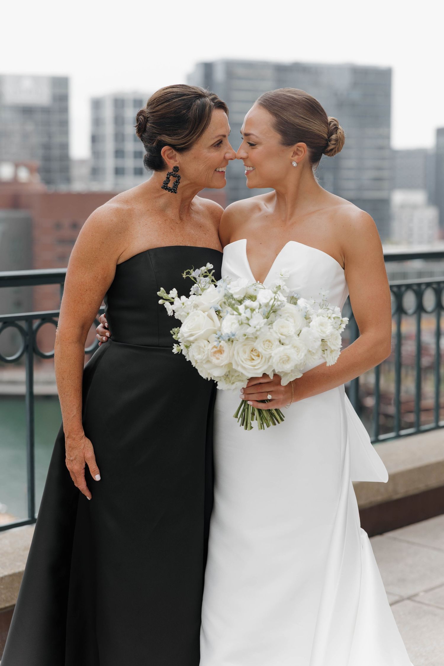 Two people in black and white formal attire share intimate moments on a rooftop terrace with city buildings in background.
