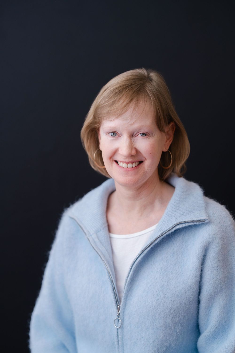 Portrait series in studio lighting featuring soft blue cardigan and white top against dark backdrop.