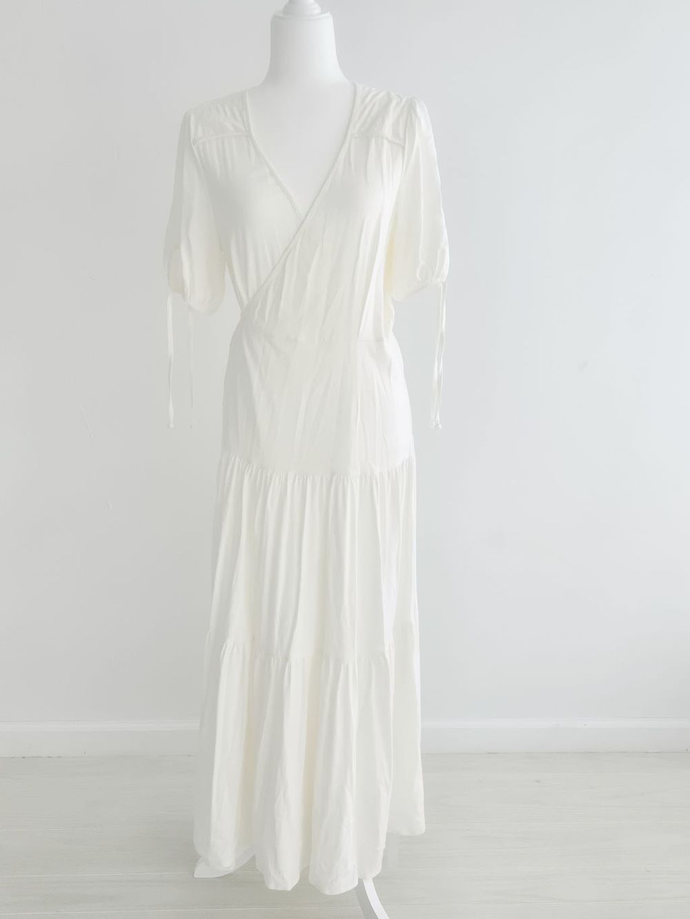 White flowy midi dress with v-neckline and long sleeves displayed on mannequin against light background.