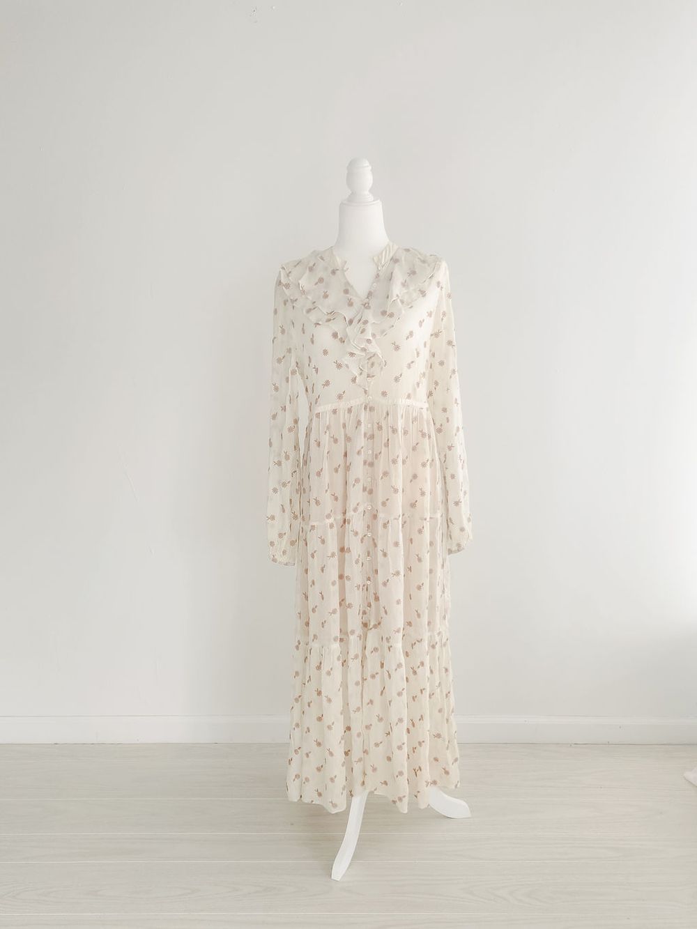 Delicate white floral print maxi dress with long sleeves and V-neckline on display form.