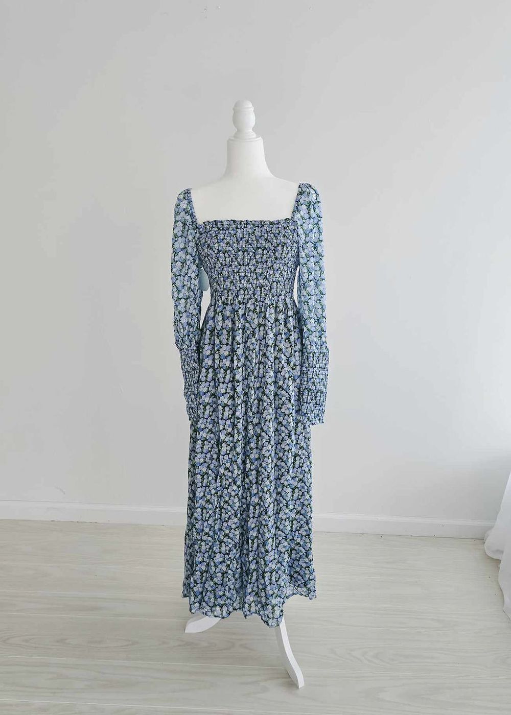 Long floral prairie dress with blue pattern, square neckline, and puff sleeves displayed on white mannequin.