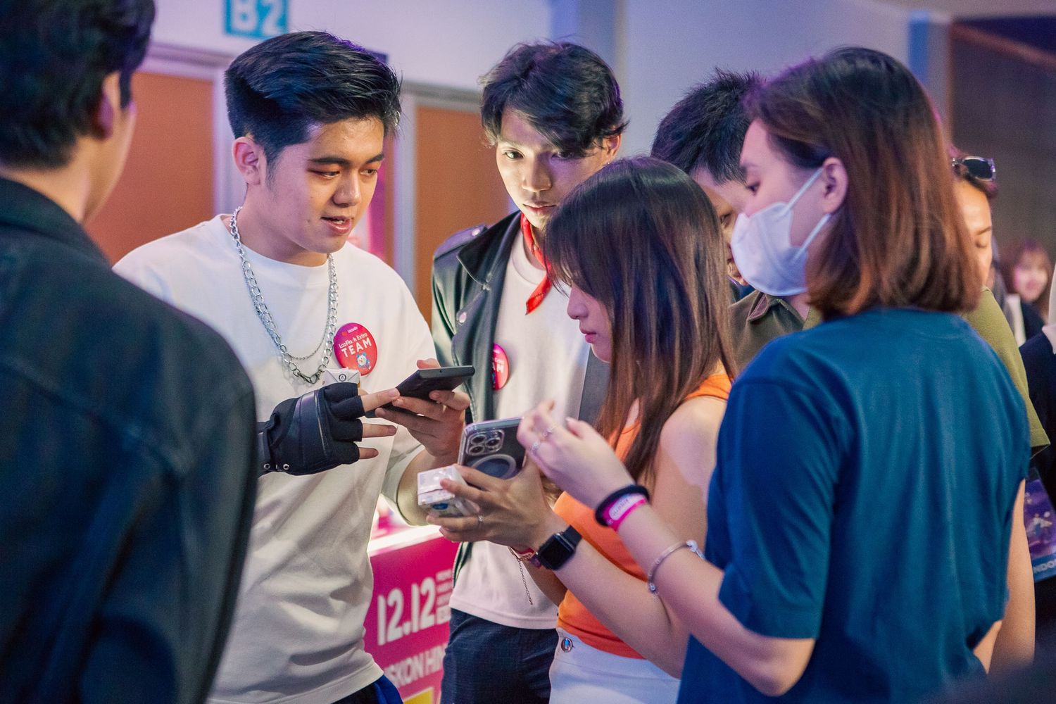 Group of young people at a 12.12 shopping event, looking at smartphones and sharing content together.