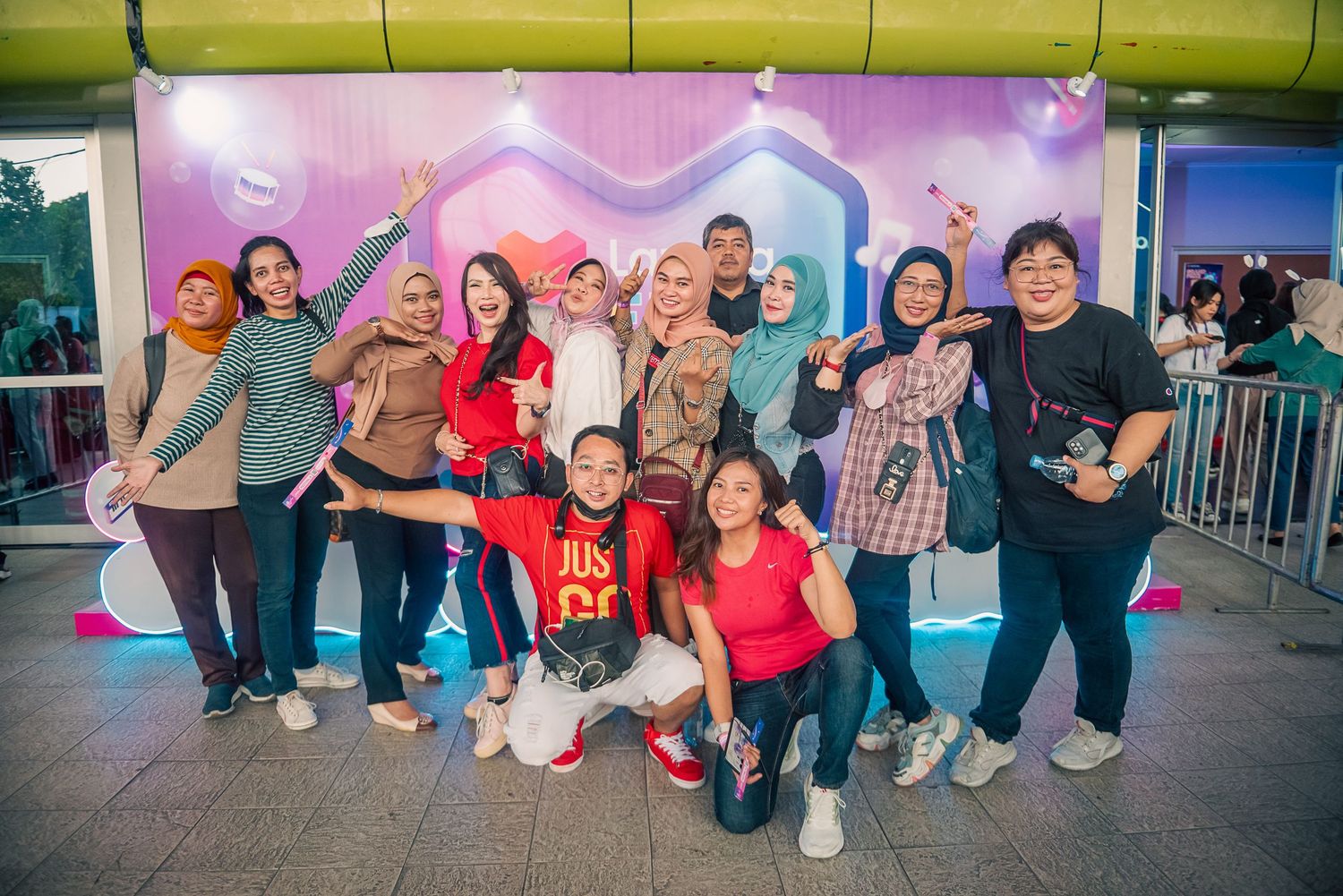 Group of friends posing together at a colorful outdoor event with vibrant pink and purple backdrop at night.