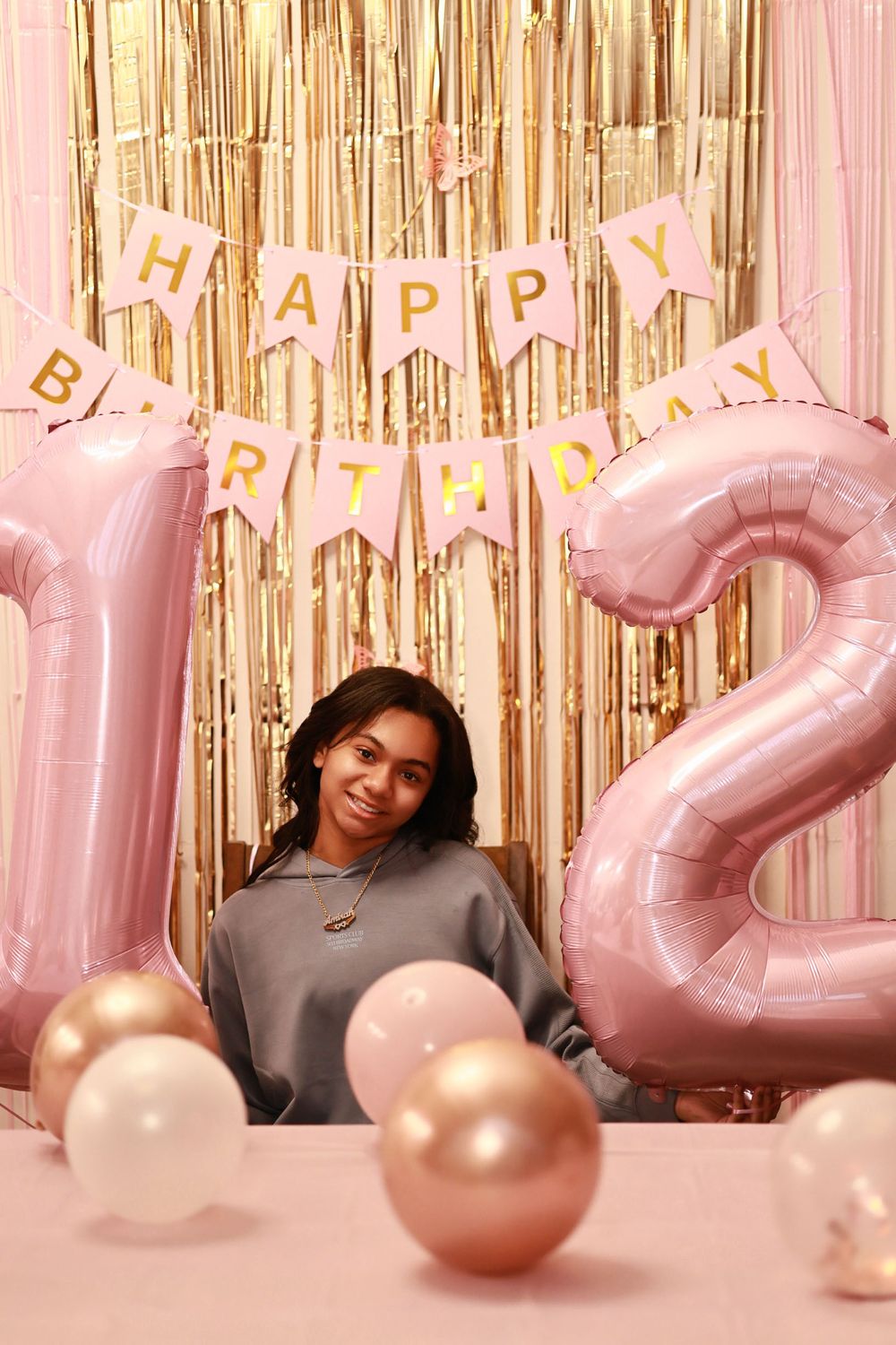 Young woman celebrating 13th birthday with pink gold balloons and Happy Birthday banner backdrop.