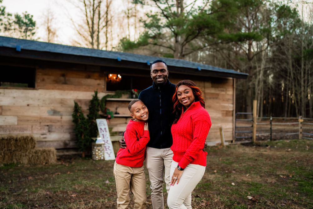 Joyful Black family posing in front of a rustic wooden cabin wearing coordinated red and khaki outfits.