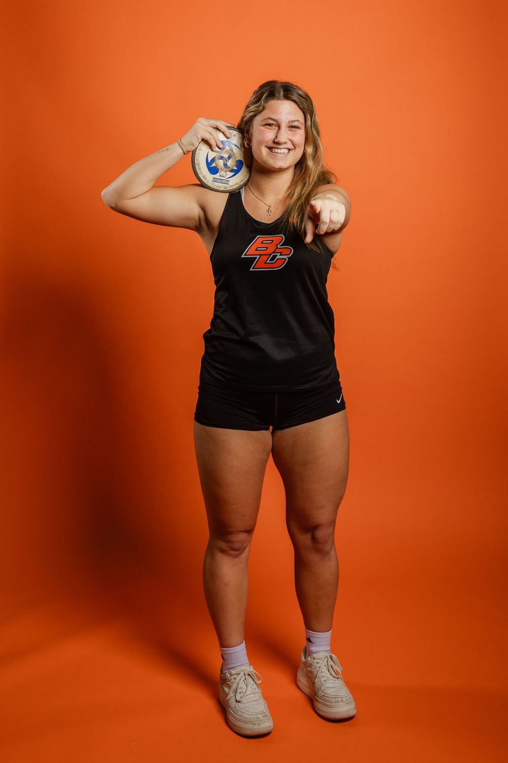 Athletic person in black tank top with number 45 holds a volleyball against orange background.