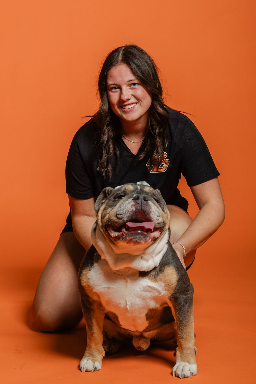 A happy bulldog poses with someone against an orange studio backdrop.