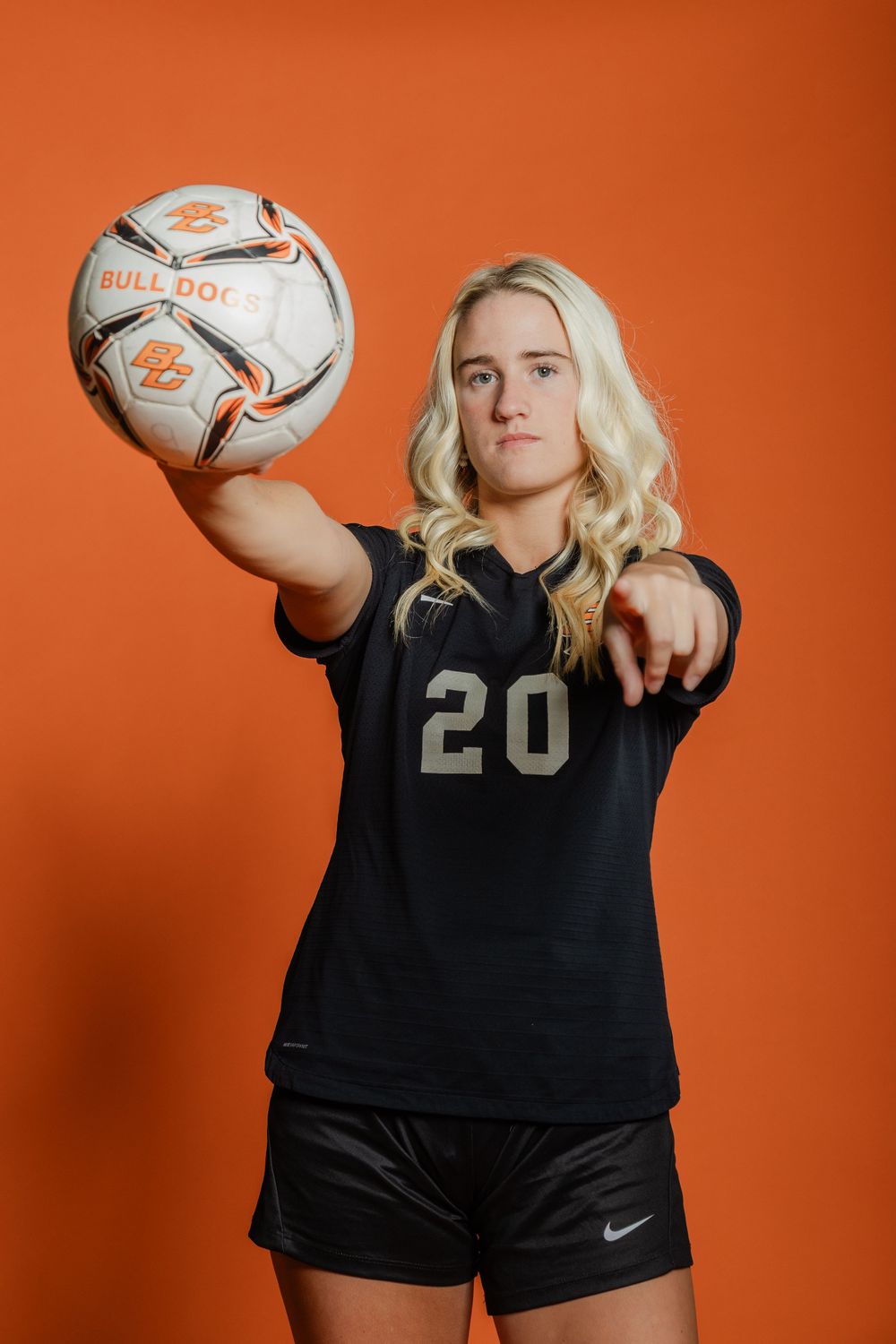 Soccer player wearing number 20 black jersey demonstrates ball control against orange backdrop.