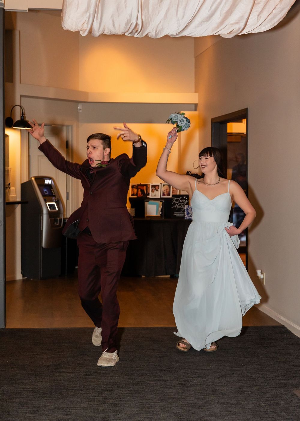 Bride in white gown and groom in burgundy suit make a grand entrance, dancing joyfully at their wedding reception.