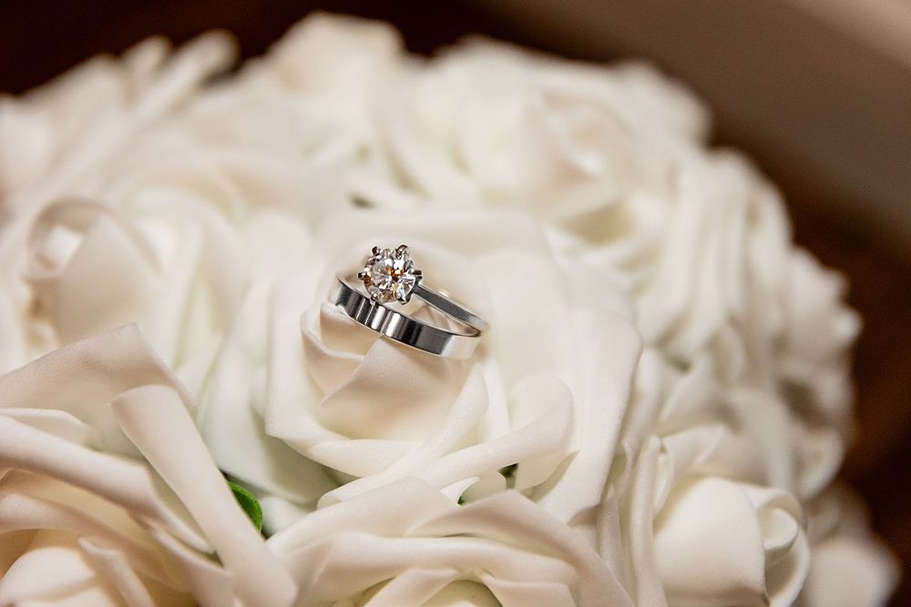 Diamond engagement ring and wedding band resting on white roses bouquet, elegant bridal jewelry close-up.