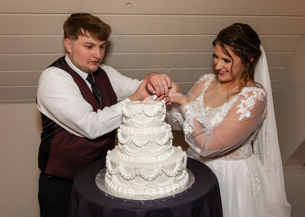 Bride and groom cutting their white tiered wedding cake together at their reception.